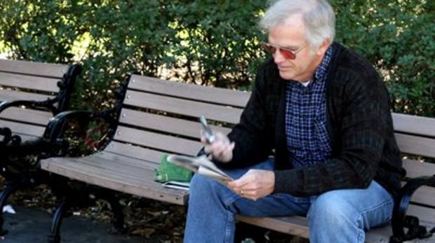 пожилой мужчина сидит на скамейке в парке с газетой в руках
