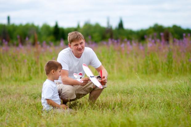 Father and son launch plane model in summer field
