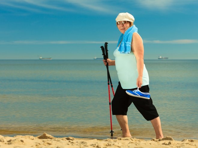 женщина занимается скандинавской ходьбой на пляже
