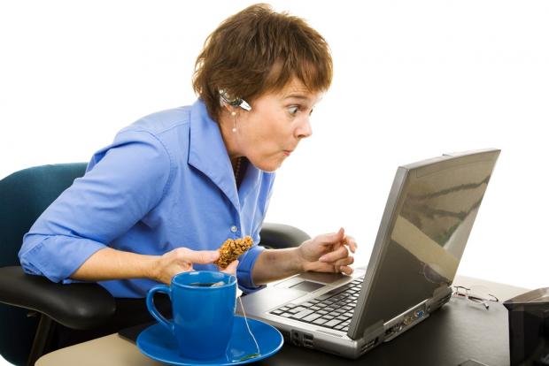 женщина ест и что-то интересное читает на экране ноутбука