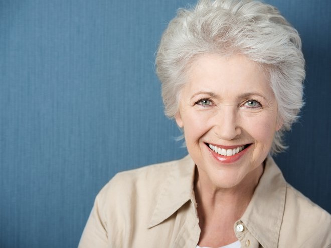 Beautiful elegant elderly lady with a lively smile looking directly at the camera while posing against a green background with copyspace
