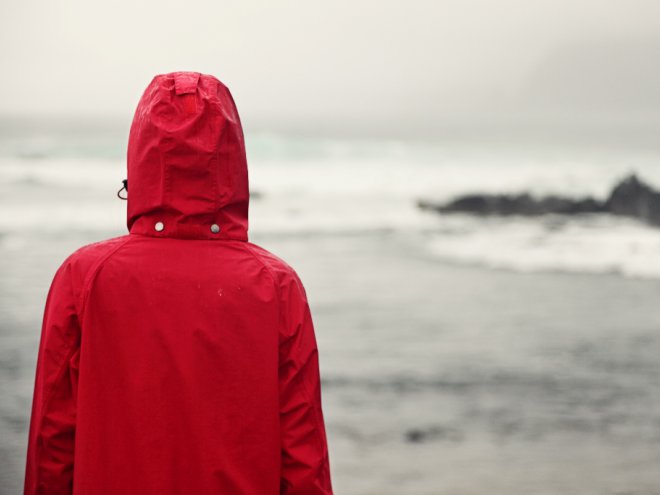 человек в красной куртке смотрит на море 