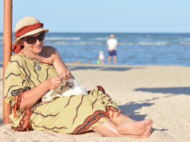зрелая женщина на пляже с рукоделием